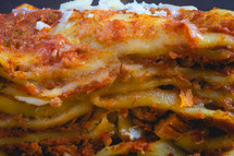 Close up view from a home made Lasagna, on a wooden table, and a dark background.
