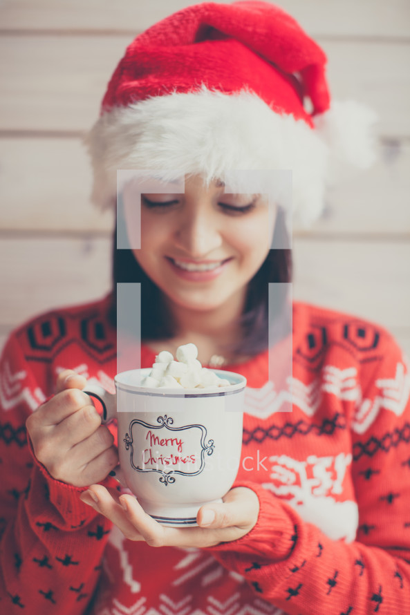 a woman in a Santa hat holding a mug of hot cocoa 