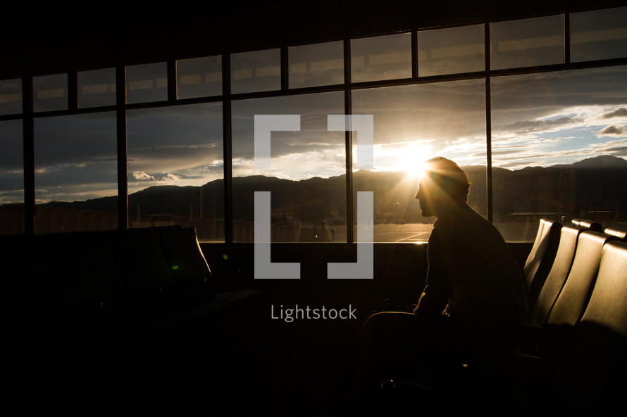 Silhouette of a man sitting by an airport window at sunrise.