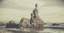 A man standing on a rock formation in the ocean. 