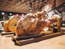 Jamon serrano. Traditional Spanish ham in the market close up. Pork leg ham on table. Meat in restaurant interior. Whole jamon on stand. Selective focus. Gourmet ham. Shallow DOF. Copy space.