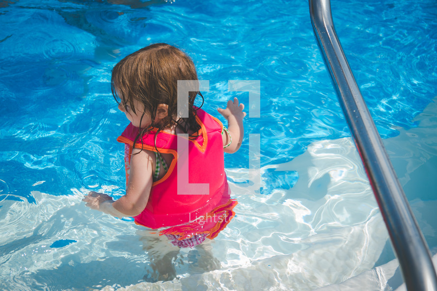 a toddler girl in a life vest in a swimming pool 