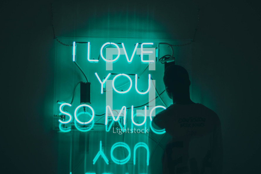a man standing near a neon sign that reads I love you so much 