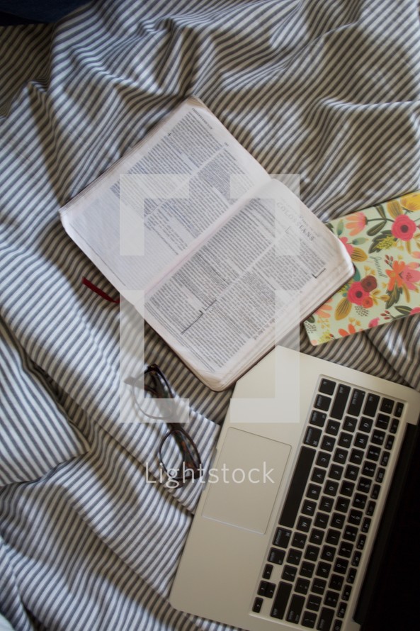 laptop computer, reading glasses, open Bible, on a bed 