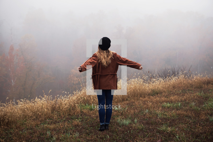 a woman standing on a foggy hill with outstretched arms 