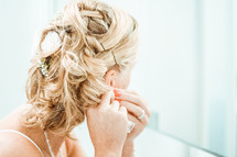 A bride putting on her earrings, preparing for her wedding.