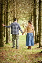 a couple walking holding hands through a forest  (vertical)
