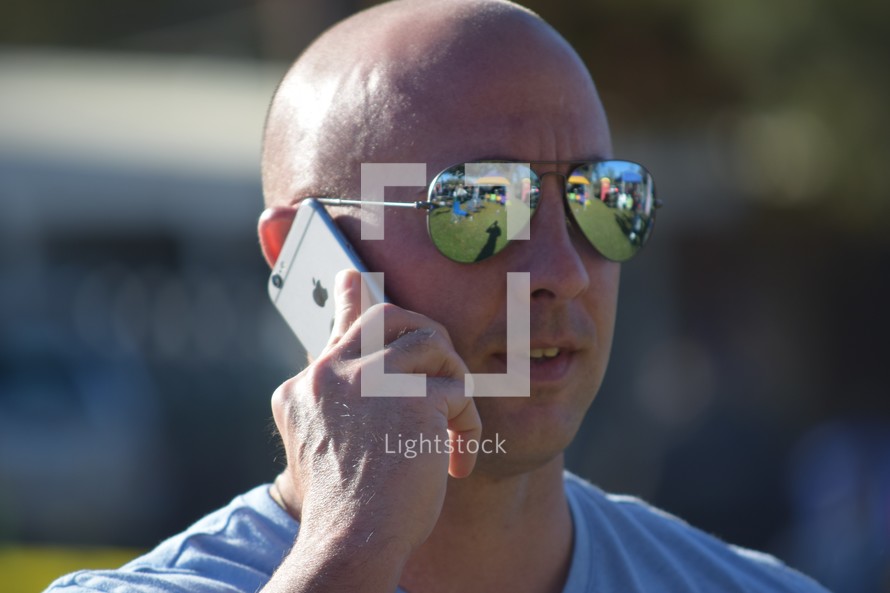 a man having a cellphone conversation with reflection in his sunglasses 