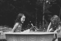 Two little girls playing in a plastic swimming pool.