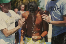Two pastors lift a teen from a baptismal pool.