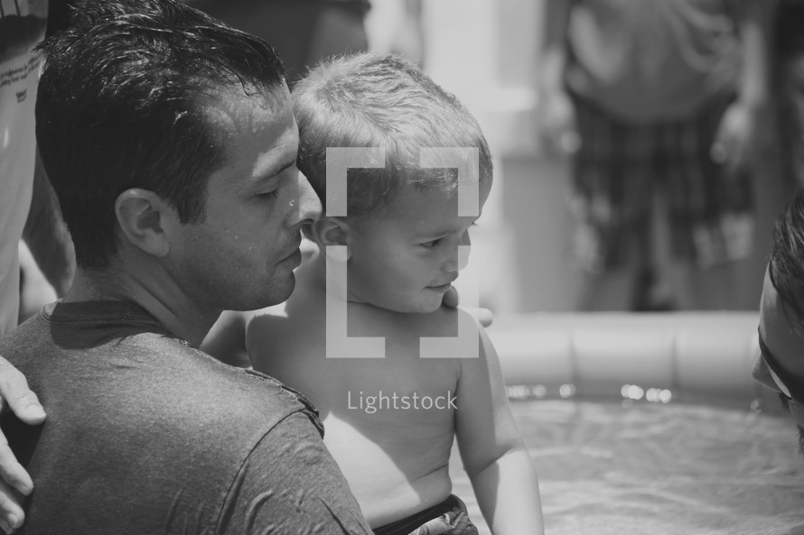 A man holds a little boy next to a baptismal pool.