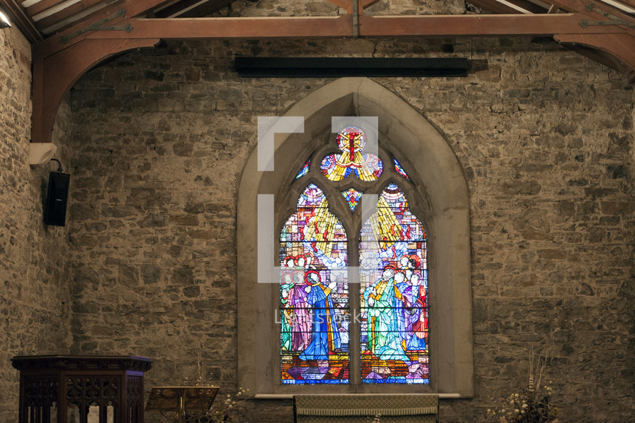 A stain glass window in a stone church sanctuary.