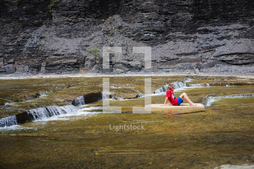 a boy sitting on a dry rock on a river bed 