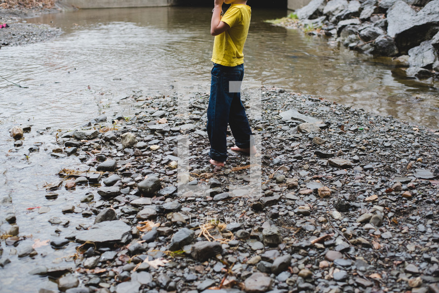 a barefoot boy skipping rocks in a stream 