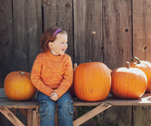 a child sitting with pumpkins 
