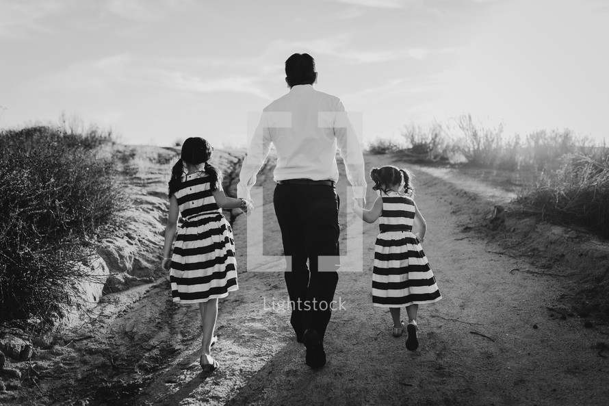 a father holding hands with his daughters as they walk up a sand dune 