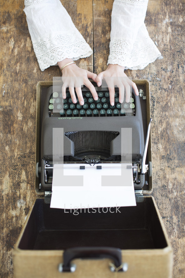 Hands typing on a vintage typewriter in a case.
