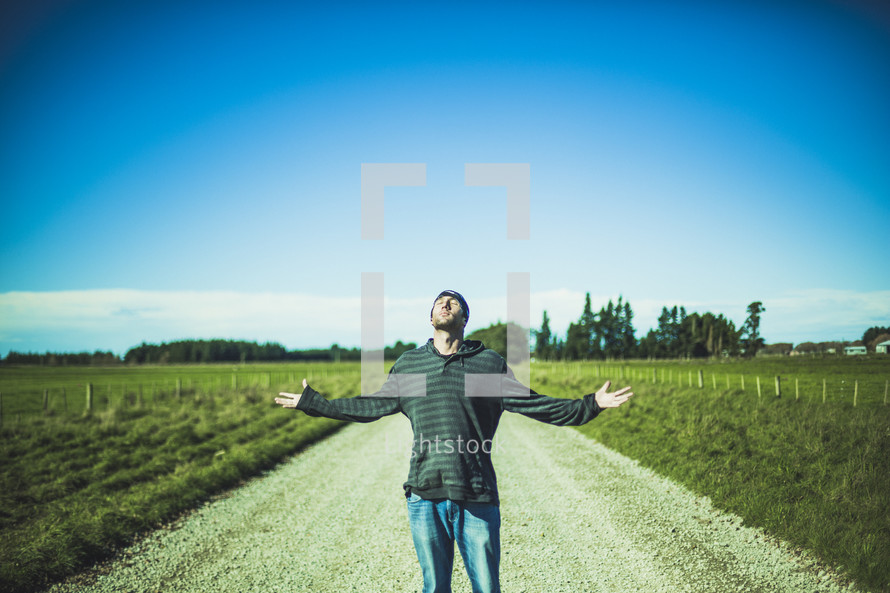 man standing in the middle of a dirt road with his hands raised 
