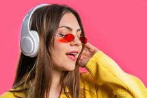 Positive woman listening music, enjoying with headphones on pink studio background. Radio, wireless modern sound technology, online player. High quality