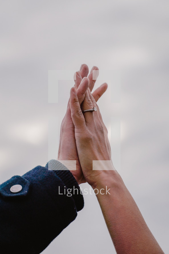 Close up of an engaged couple holding hands in the air.