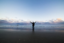 Man on a beach with arms raised toward sky.