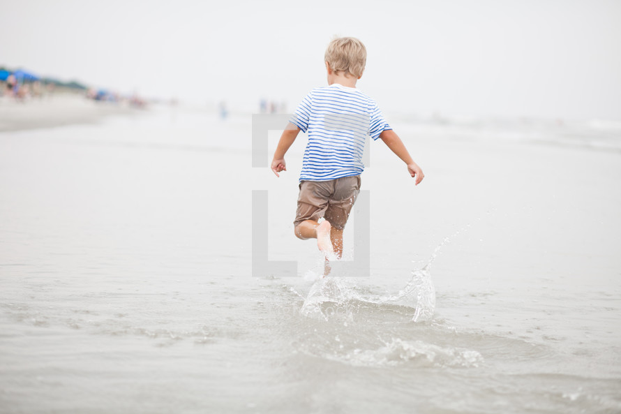 Boy running through the ocean water at the beach.