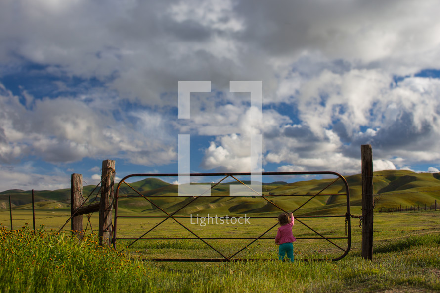 toddler girl standing at a ranch gate 