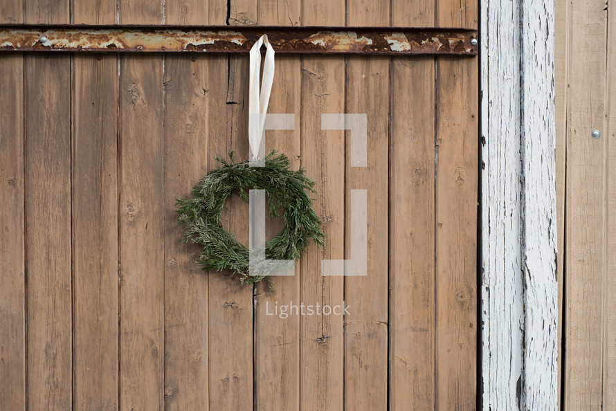 An evergreen wreath hanging on a wooden gate.