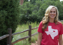 woman with a Texas t-shirt standing by a fence 