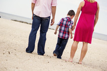 Back view of father, boy and mother walking on white beach