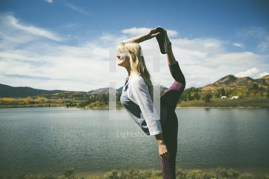 a woman stretching and doing yoga by a lake 