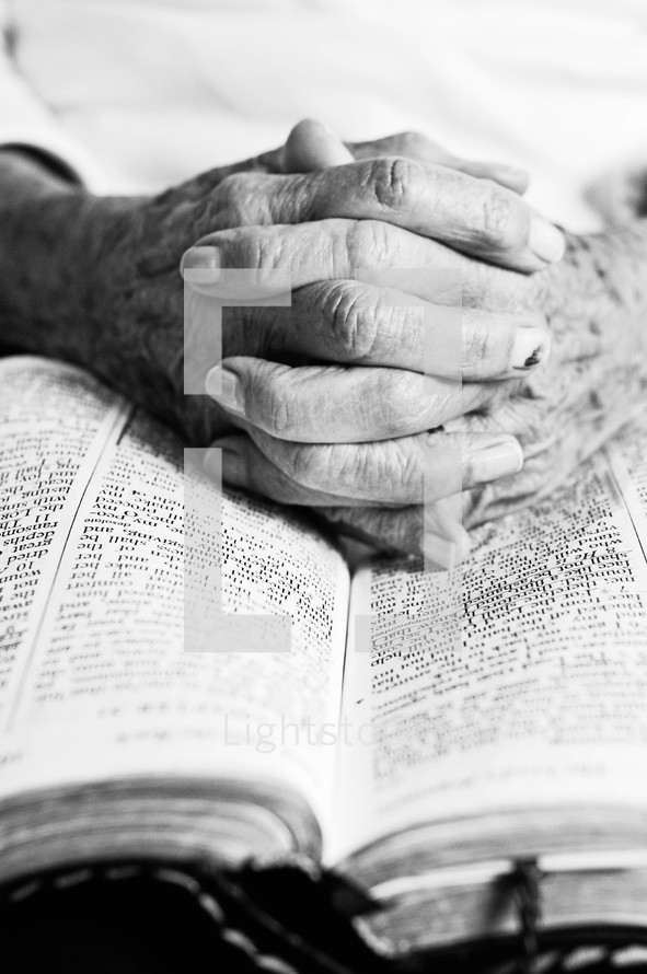 Elderly hands interlaced on an open bible.