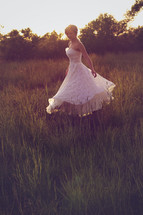 Woman in white dress twirling in a field of tall grass.