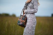 a woman standing in a field holding a purse 