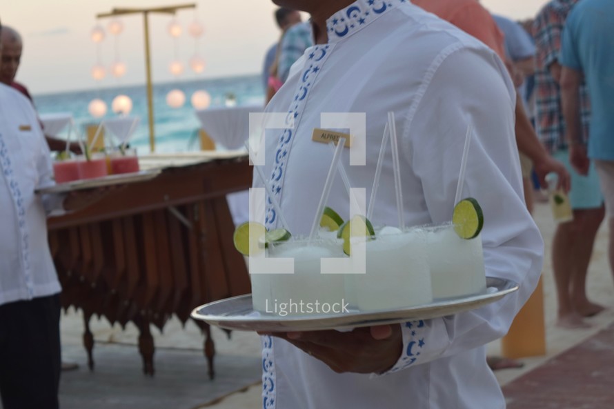 A server carrying a tray of margaritas at a reception on the beach 