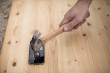 Hand holding a hammer, smashing an iphone on a wood board.