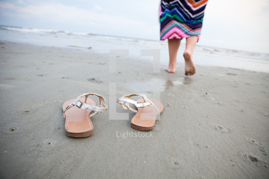 woman walking barefoot in the sand on a beach and a pair of flip flops 