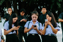 Asian men and women in uniforms texting on cellphones 