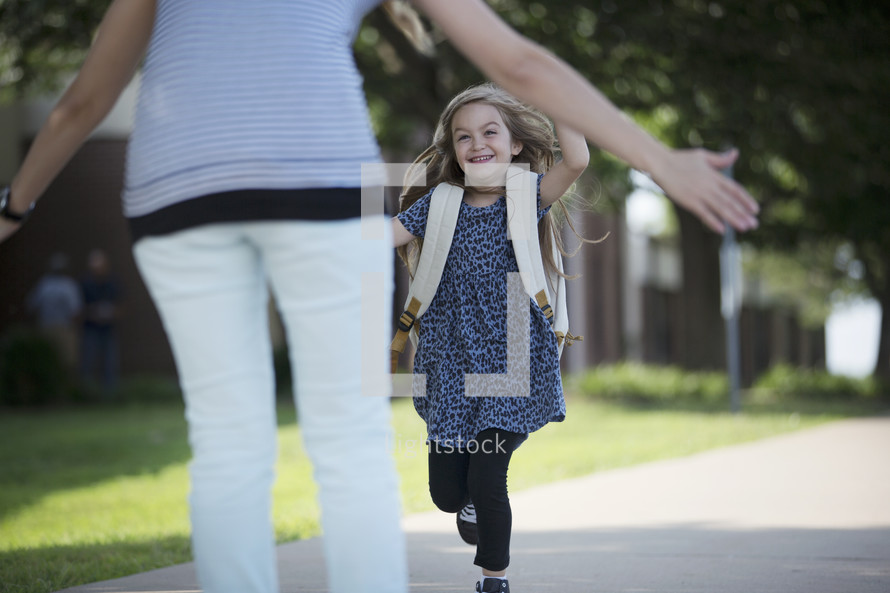 a little girl with a book bag running to hug mom 