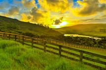 sunrise over a green pasture and fence line 