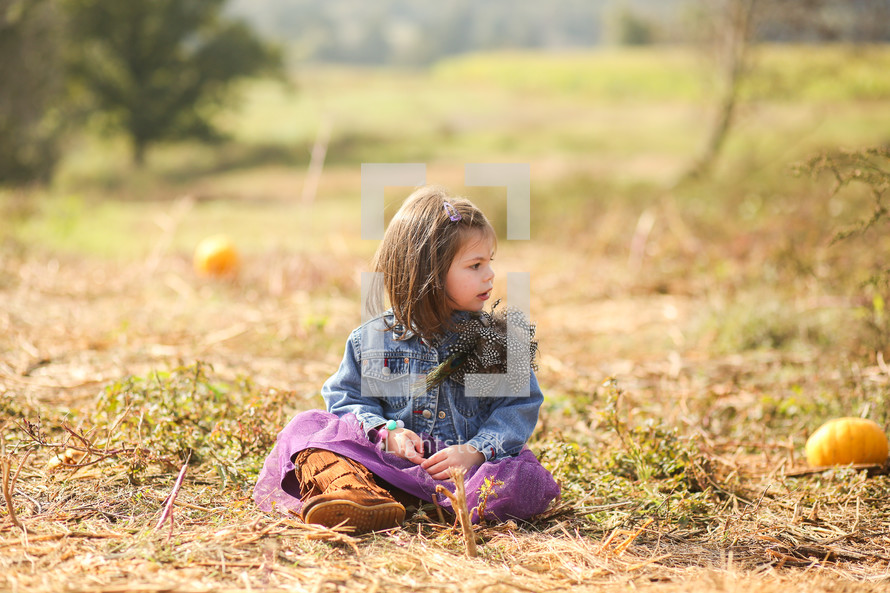 girl child sitting in a pumpkin patch 