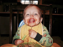 A messy toddler boy eating spaghetti in a high-chair 