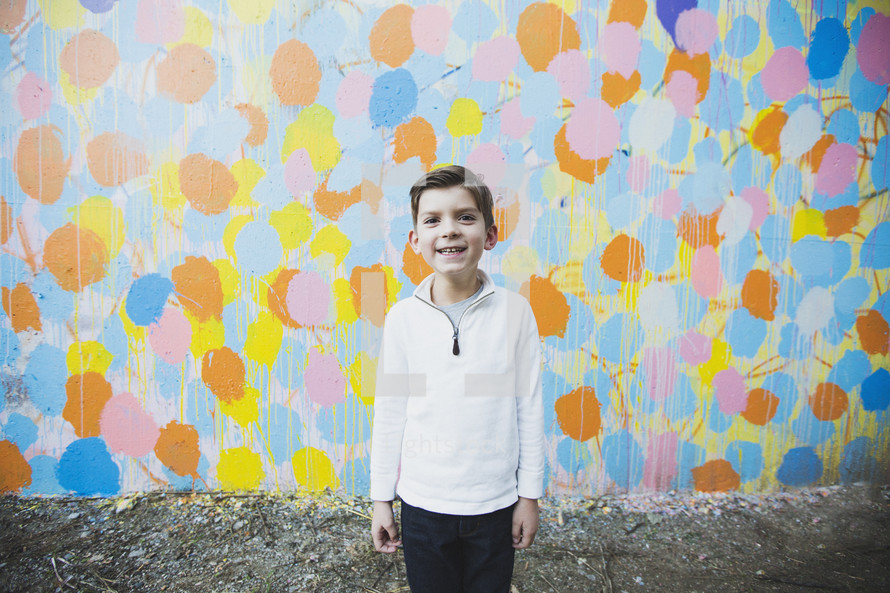 a boy child standing in front of a colorful wall 
