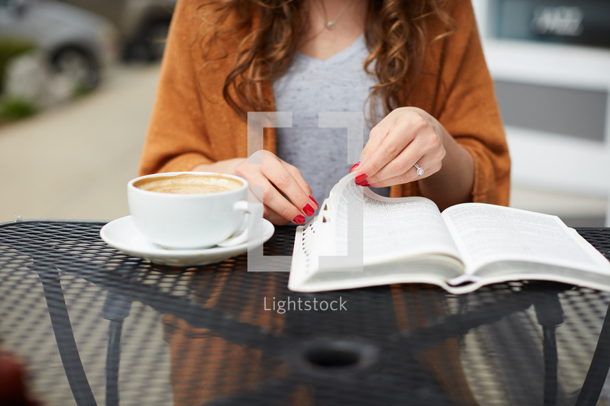 a woman sitting at an outdoor table reading a Bible 