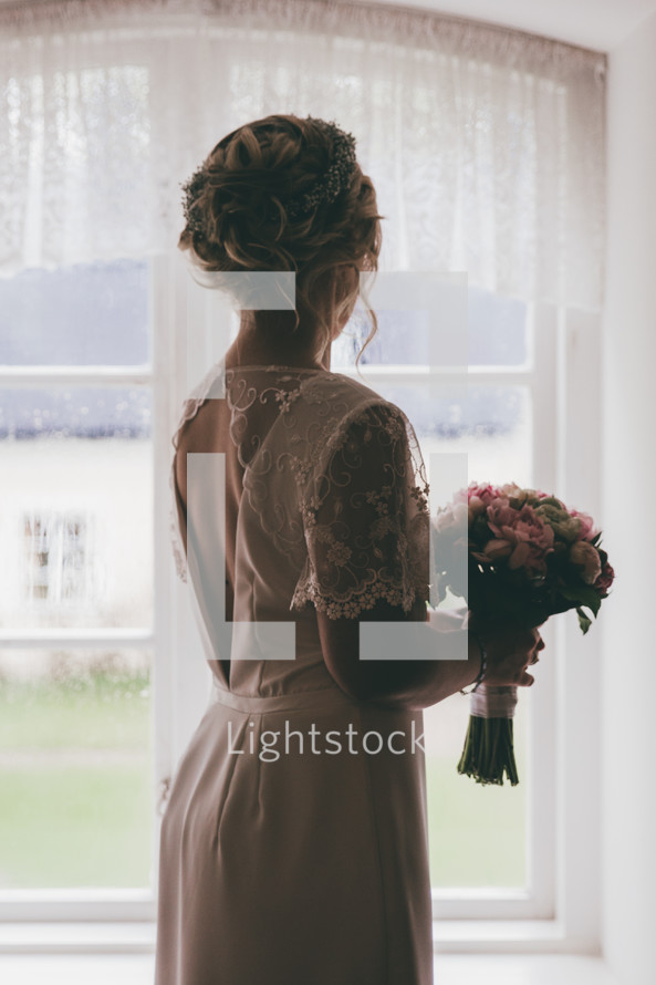 a bride standing in a window holding a bouquet 