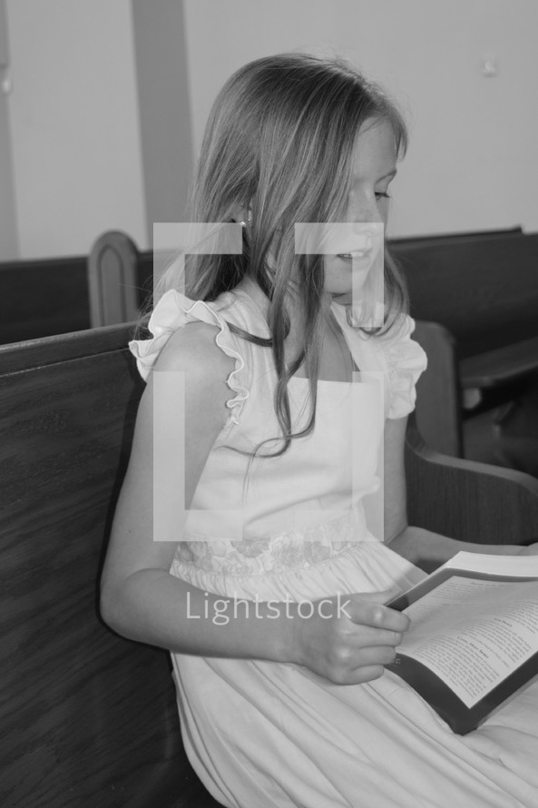 a little girl singing from a hymnal in a church pew 