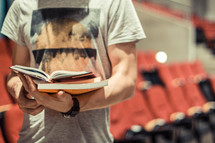 Man reading a book in an auditorium.