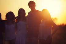friends standing outdoors embracing at sunset 