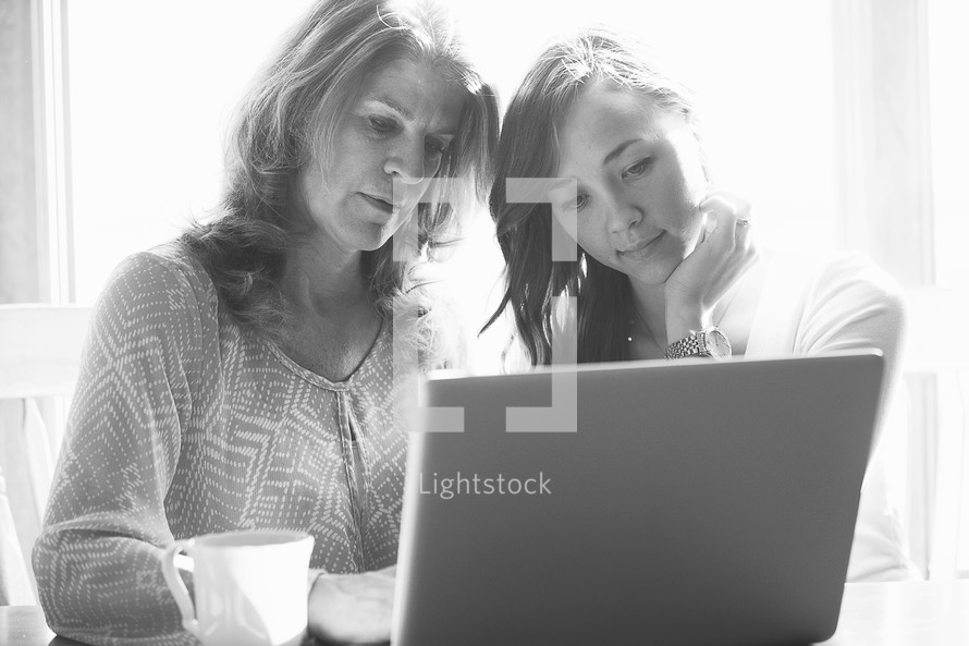Woman and her daughter working at a laptop computer with coffee in the morning sun.