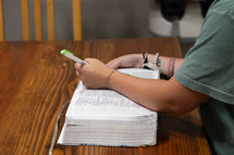 Woman in green shirt sitting at kitchen table opening Bible during Bible study time in her discipleship group, highlighting